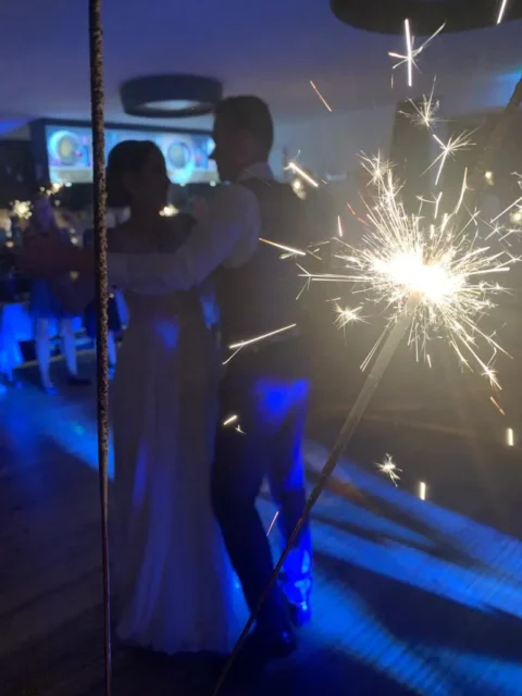 Brautpaar tanzt im dunklen Raum, umgeben von funkelnden Wunderkerzen und blauen Lichtern.