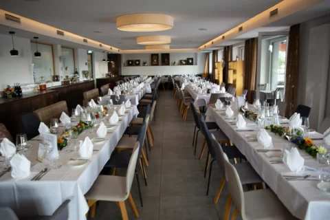 Elegant gedecktes Restaurant mit langen Tafeln, weißen Tischdecken und gefalteten Servietten, bereit für eine Veranstaltung.
