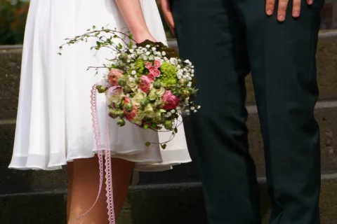 Nahaufnahme eines Brautpaars: Braut mit Blumenstrauß und Bräutigam in dunkler Hose.