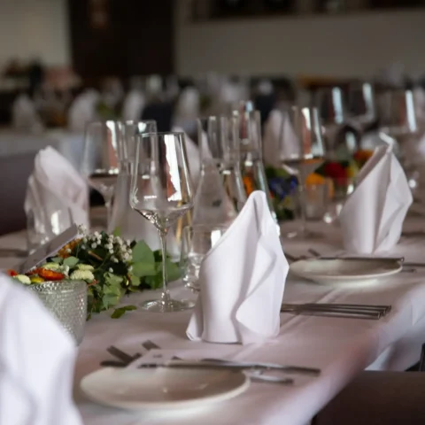 Elegant gedeckter Tisch in einem Restaurant mit Weingläsern, Besteck, Servietten und Blumendekoration.