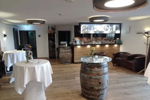 Gemütlicher Veranstaltungsraum mit Bar, rustikalen Weinfässern als Tische und eleganter Dekoration.