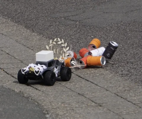 Spielzeugauto mit Deko und Doseanhänger als Hochzeitsauto auf der Straße.
