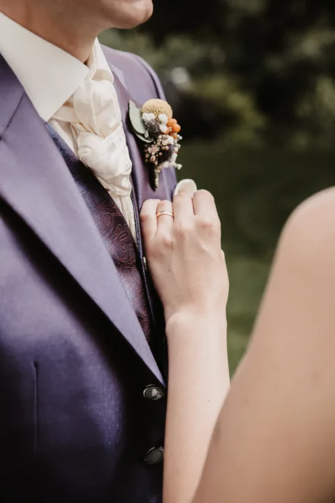 Nahaufnahme eines Hochzeitspaares, wobei die Braut den Anzug des Bräutigams richtet.