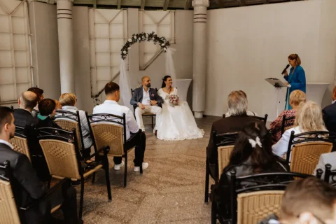 Traurednerin hält bewegende Zeremonie für Brautpaar in elegantem Ambiente vor Gästen.