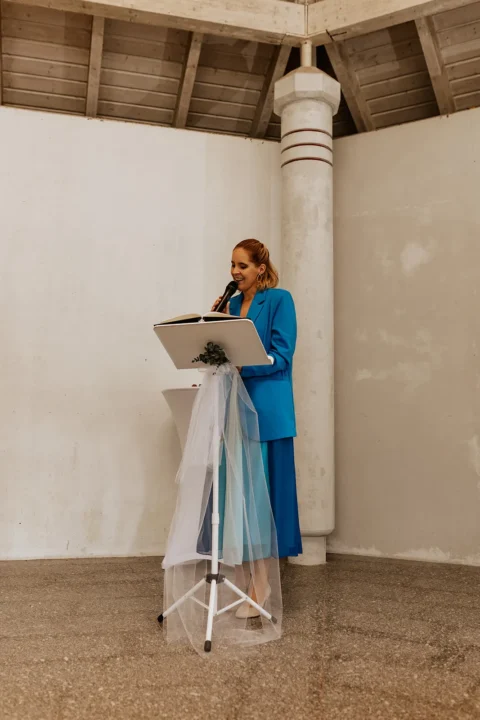 Traurednerin in blauem Anzug hält emotionale Rede am Rednerpult bei einer Hochzeitszeremonie.