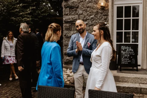 Hochzeit: Gespräch der Traurednerin mit Brautpaar vor einer Steinmauer.
