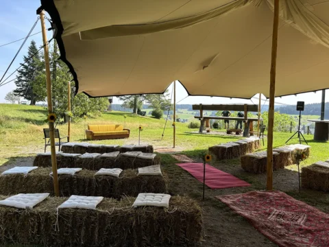 Outdoor-Hochzeitslocation mit Strohballen-Sitzen und gelbem Sofa, dekoriert für romantische Trauung im Freien.