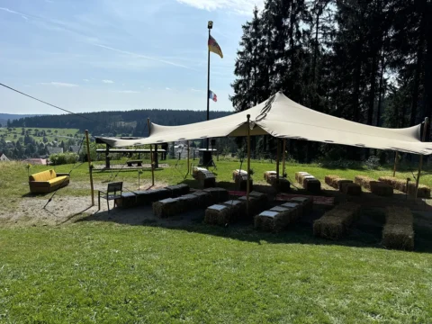 Freiluft-Trauzeremonie mit Zelt und Heuballen-Sitzplätzen, umgeben von Wald und weiter Landschaft.