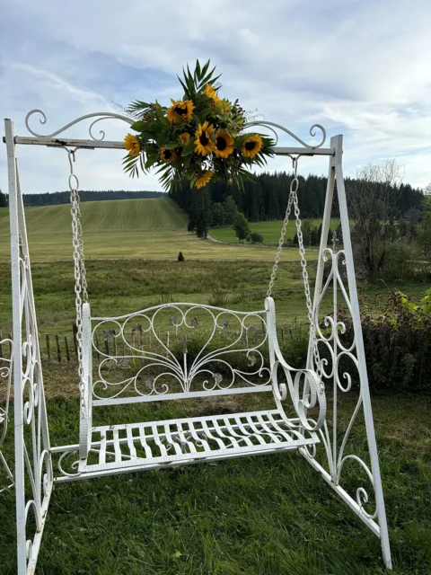 Weiße Gartenbank mit Sonnenblumen-Deko auf einer grünen Wiese, ideal für romantische Trauungen im Freien.