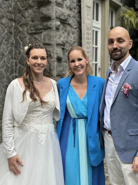 Brautpaar mit Traurednerin bei der Hochzeitszeremonie, glückliche Gesichter im Freien.