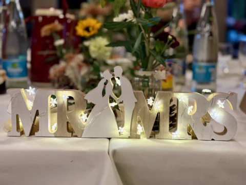 Hochzeitsdekoration mit beleuchtetem Mr & Mrs für romantische Feier im Hintergrund mit Blumen und Lichtern.